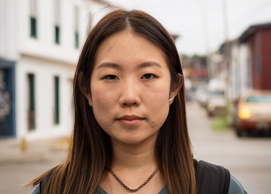 Asian woman in her 20s or 30s, smiling in front of a small town street